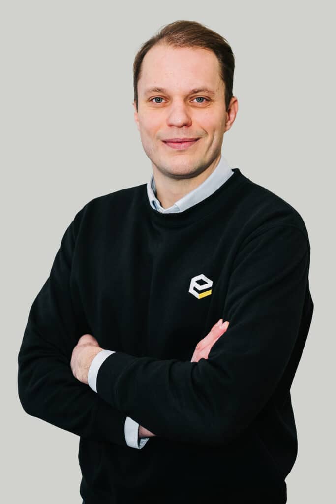 Petras Nauseda, VD för ELEMET Recycling AB, står med armarna i kors och bär en svart tröja med företagets logotyp, vilket återspeglar hans ledarskap och företagets fokus på hållbar metallåtervinning.